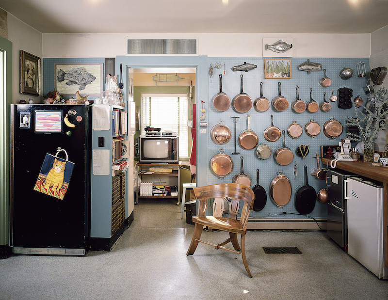 Kitchen view, west, showing copper pans and black refrigerator.